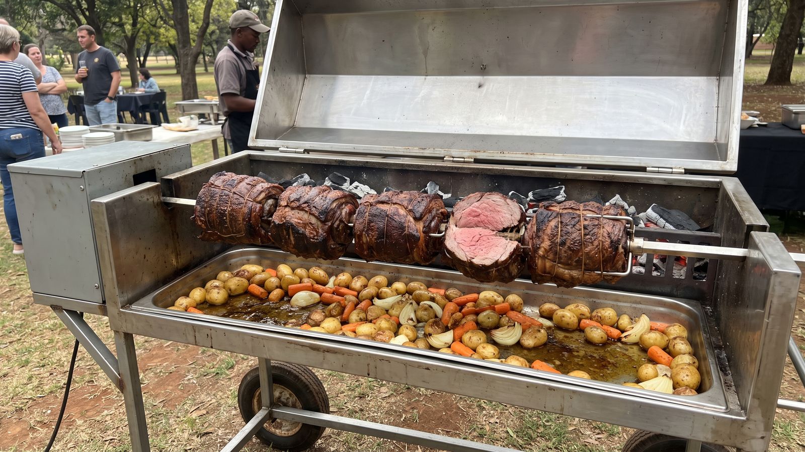 Beef spit braai: a tied beef roast on the spit over coals with sliced beef on a board