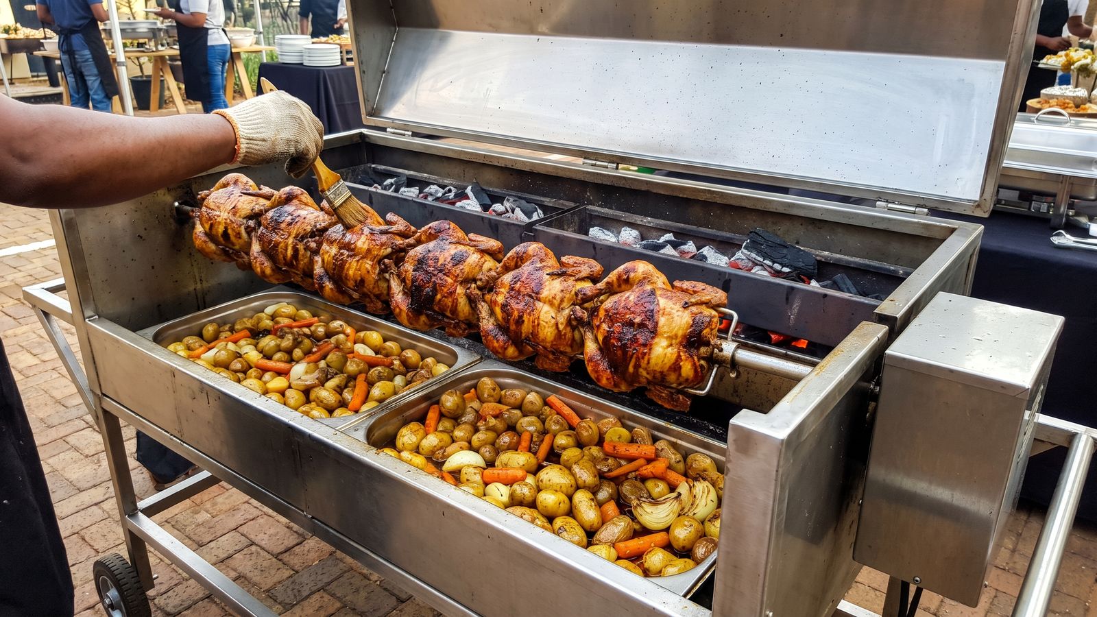 Chicken spit braai: whole chickens skewered on one spit rod over coals, being basted