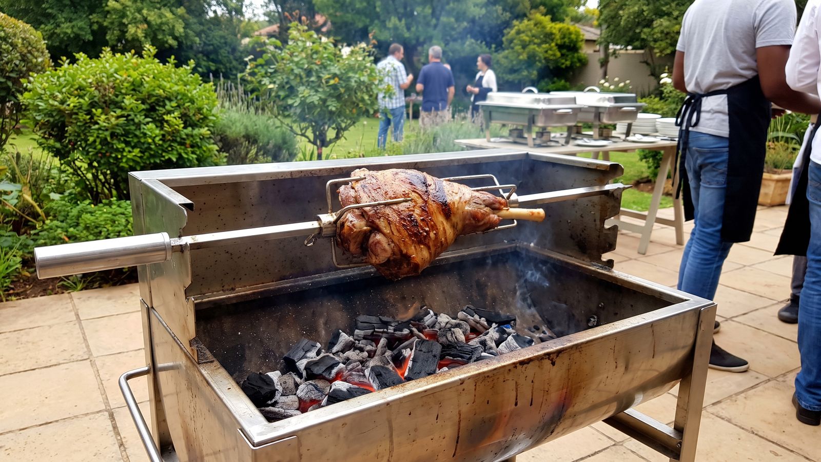 Leg of lamb on a spit: a bone-in lamb leg turning over charcoal on a small stainless rotisserie