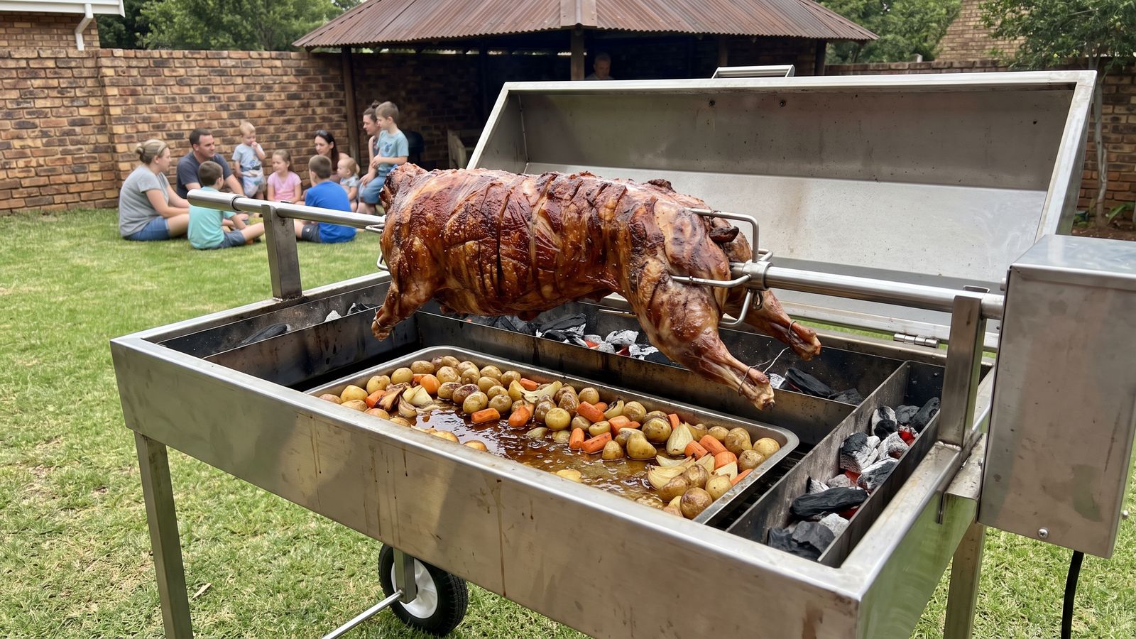 Whole lamb spit braai on a stainless machine at a family function in a back garden, the kind Spit Braai Feast caters in Brackenfell