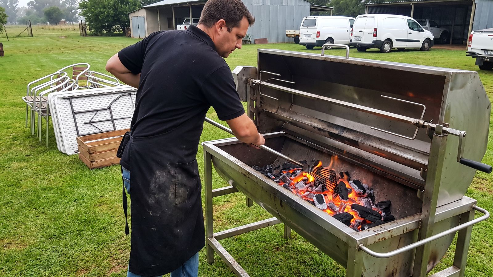 Raking fresh charcoal into the channels of a spit braai machine before a function
