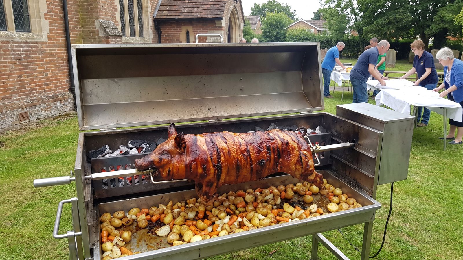 Whole pig spit braai on a stainless machine at a church-ground function, the kind Spit Braai Feast caters in Kraaifontein